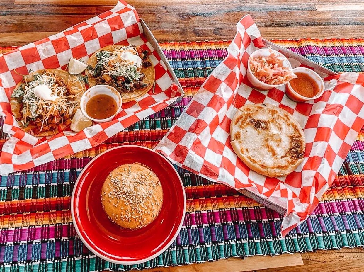 Food spread at Finca Coffee in Fitchburg with tacos, a pork pupusa, and a Salvadoran quesadilla on a colorful woven tablecloth